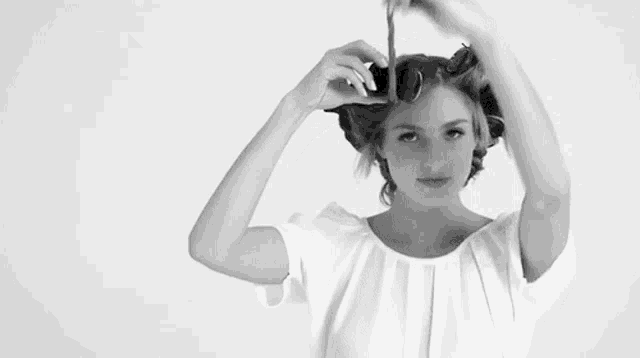 a woman in a white shirt is curling her hair with curlers .
