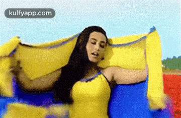 a woman in a yellow dress is holding a blue and yellow scarf .
