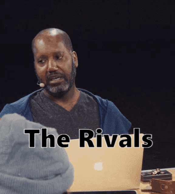 a man sitting in front of an apple laptop with the words the rivals written on the screen