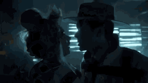 a man in a fedora is holding a woman in a dark room .