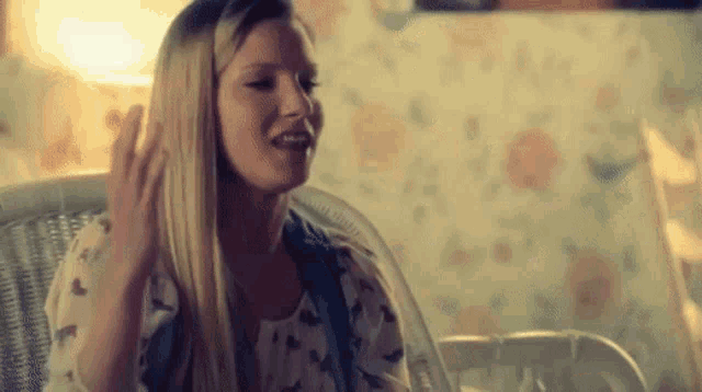 a woman with long blonde hair is sitting in a wicker chair and smiling