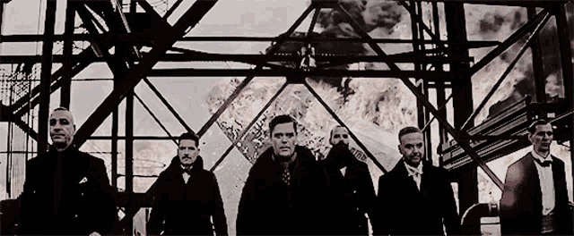 a group of men are standing in front of a building with a fire behind them