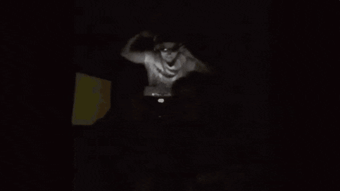 a man is sitting in a chair in a dark room while another man is standing in the background .