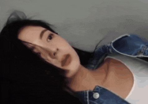 a woman with long black hair is wearing a white tank top and a blue jacket .