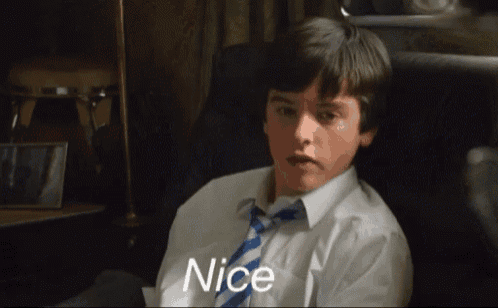 a boy in a white shirt and tie is sitting in a chair and the word nice is on the screen behind him
