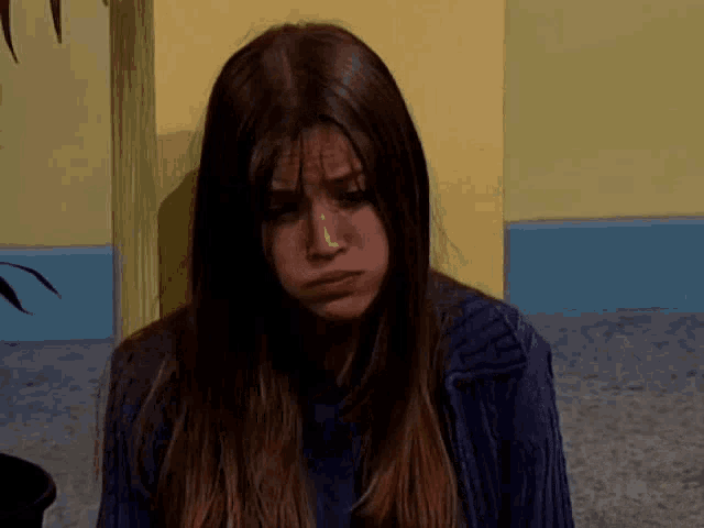 a woman with long brown hair and a blue sweater looks sad