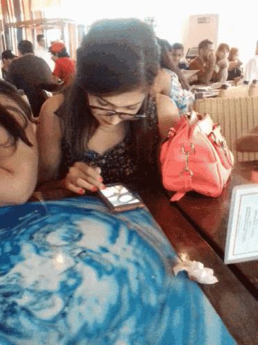 a woman sitting at a table with a pink purse looking at her phone