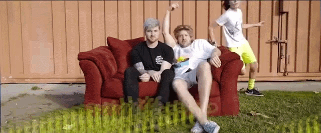 three men are sitting on a red couch in front of a wall