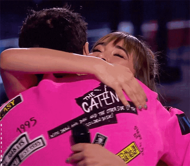 a woman hugging a man wearing a pink shirt that says the caten on it