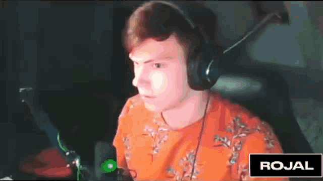a man wearing headphones and an orange shirt is sitting in front of a microphone and a sign that says rojal .