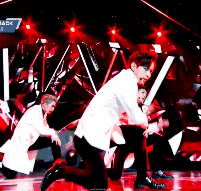 a group of men are dancing on a stage in front of a red background .
