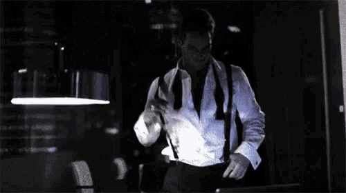 a man in a white shirt and black suspenders is standing in the dark