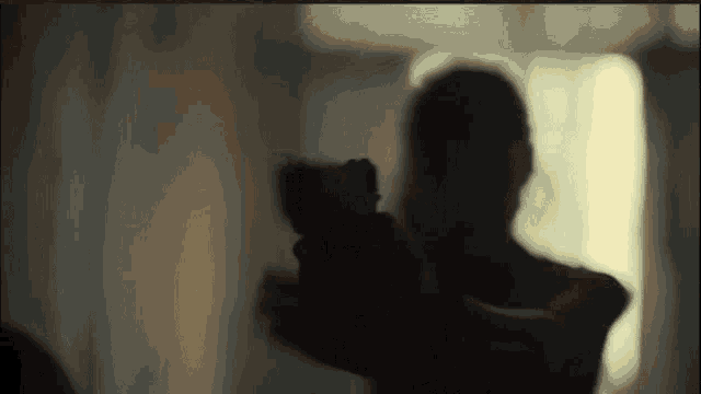 a silhouette of a man holding a gun in front of a window
