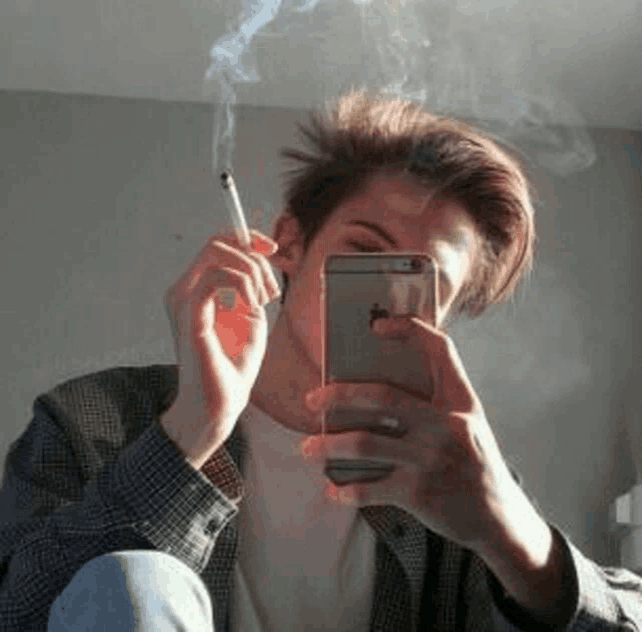 a young man is smoking a cigarette and taking a picture of himself with his phone .