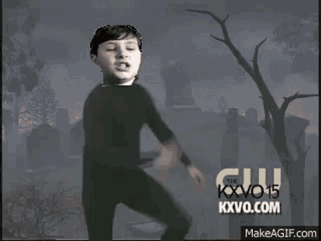 a man in a black suit is dancing in front of a cemetery with trees .