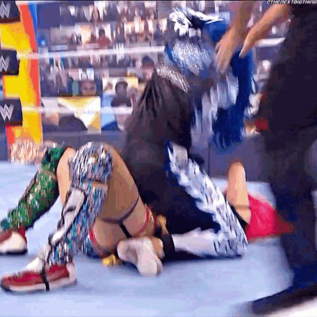 a wrestler is laying on the ground in a wrestling ring while another wrestler looks on .