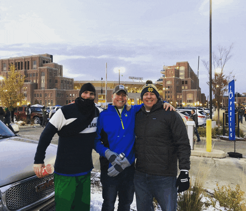 three men pose for a picture in front of a gm truck in a parking lot