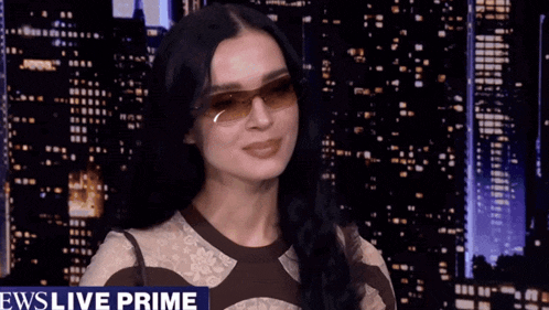 a woman wearing sunglasses is standing in front of a news live prime sign