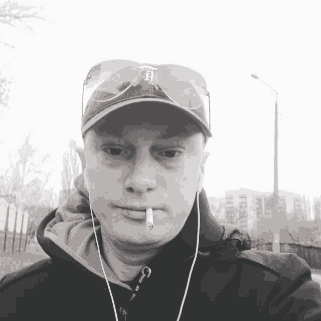 a man with a cigarette in his mouth wearing sunglasses and a hat with the letter e on it