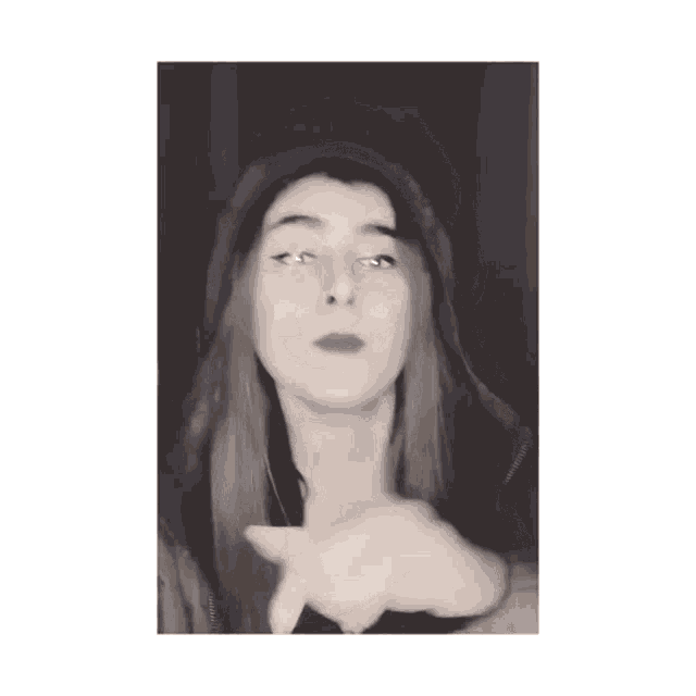 a black and white photo of a woman wearing a hoodie and making a peace sign .