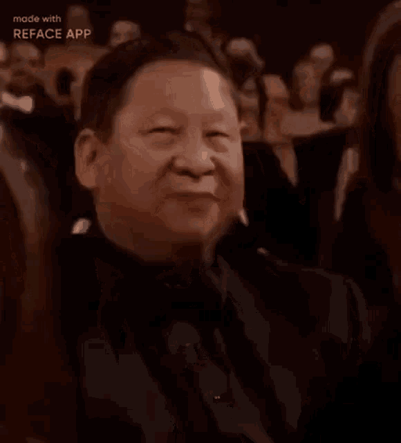 a man is smiling while sitting in a crowd of people applauding .