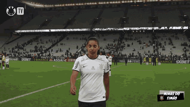 a woman stands on a soccer field with minas do timão written in the corner
