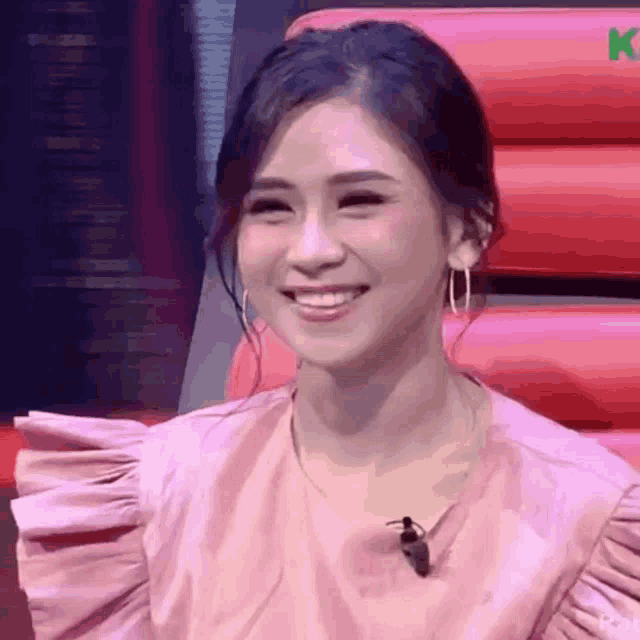 a woman wearing a pink shirt and earrings is smiling while sitting in a chair .