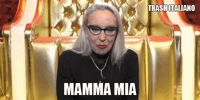 a woman wearing glasses and a black shirt is sitting in a chair with the words mamma mia written on it .