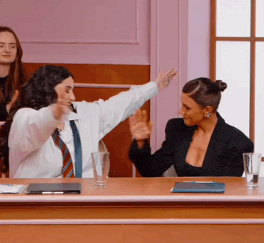 two women sitting at a table with their arms outstretched