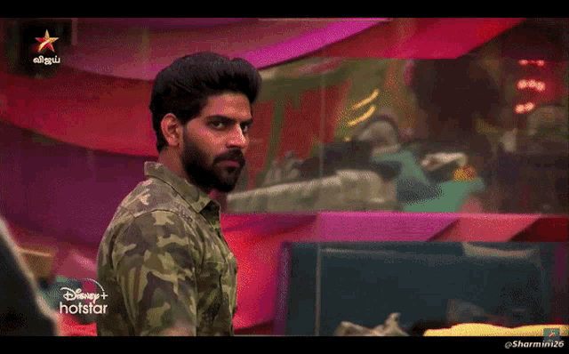 a man in a camo shirt is standing in front of a hotstar logo