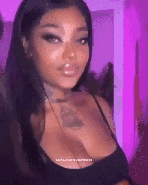 a woman with a tattoo on her chest is standing in front of a purple wall .