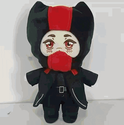 a stuffed animal with a red scarf around its neck and a black hood is standing on a white surface .