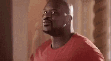a man in a red shirt is standing in a room and looking up .