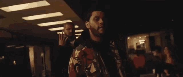 a man with a beard is standing in a dark room with a woman standing behind him .