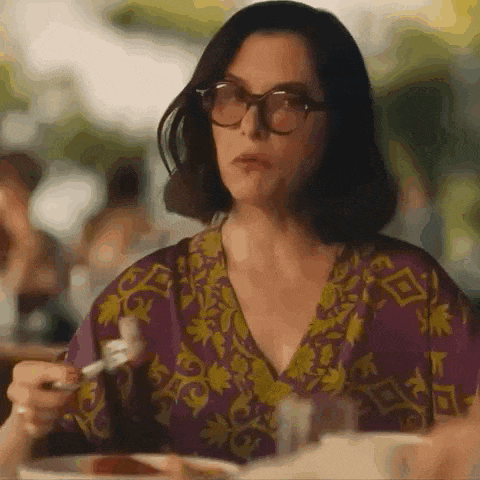 a woman wearing glasses and a purple dress is sitting at a table eating food .