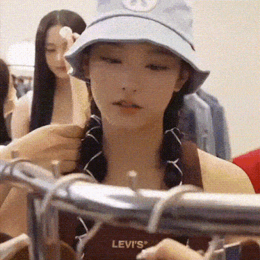 a woman wearing a hat and a levi 's shirt is standing in a clothing store .