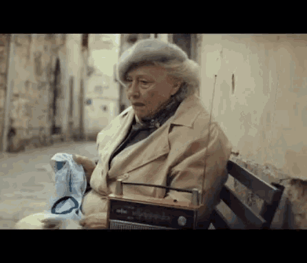 an elderly woman sits on a bench with a radio