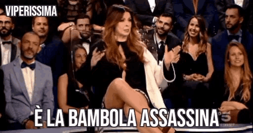 a woman is sitting in front of a crowd with the words e la bambola assassina written above her