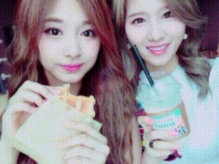 two young women are eating a sandwich and drinking a beverage .