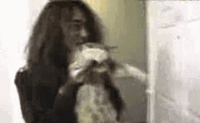 a woman with long hair is holding a cat in her arms in front of a refrigerator .