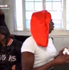 a woman wearing a red head scarf is sitting in front of a window holding a controller .