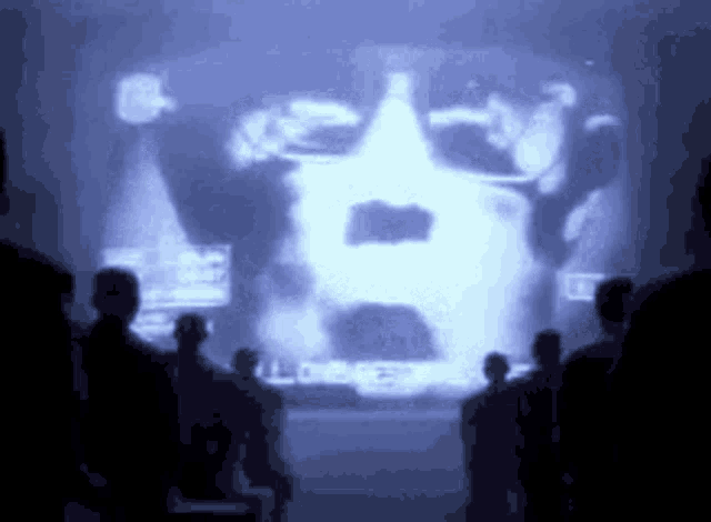 a group of people are standing in front of a large screen with a picture of a man 's face on it