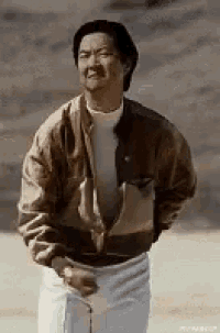 a man wearing a brown jacket and white shorts is standing in the sand .