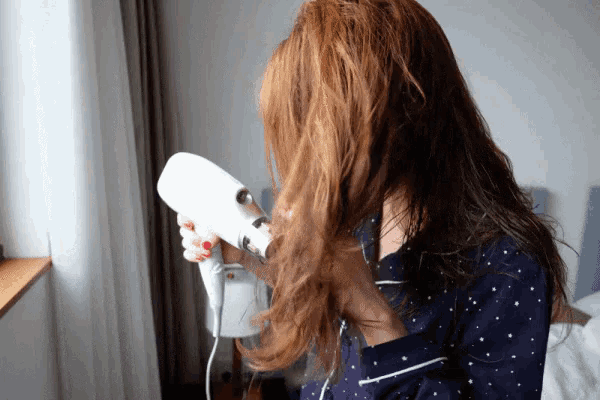 a woman is blow drying her hair with a white hair dryer