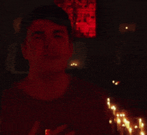 a man stands in front of a row of lit candles with his eyes closed