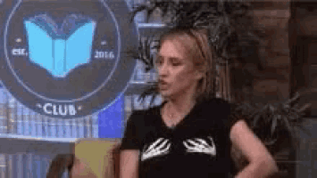 a woman wearing a black shirt with skeleton hands on it is sitting on a couch in front of a club logo .