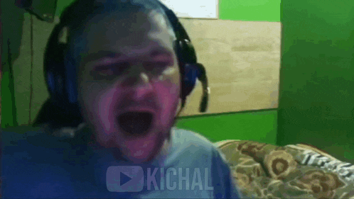 a man wearing headphones is screaming in front of a green wall .
