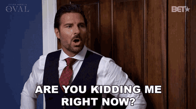 a man in a suit and tie is asking if he is kidding me right now