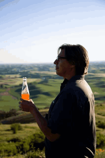 a man holding a bottle of mirinda in front of a lush green field