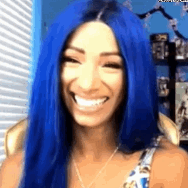 a woman with long blue hair is smiling and wearing a necklace .
